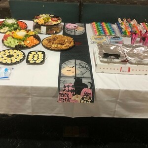 Large table containing a variety of food and desserts decorated with a Halloween banner