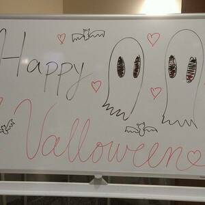 Whiteboard sign reading Happy Valloween with doodles of ghosts, bats, and hearts