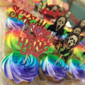 Close up shot of rainbow-frosted cupcakes with toppers from the movie Scream