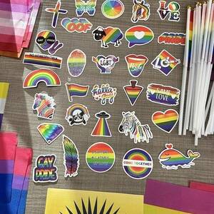 Close up photo of various rainbow pride stickers sitting amongst several types of mini pride flags