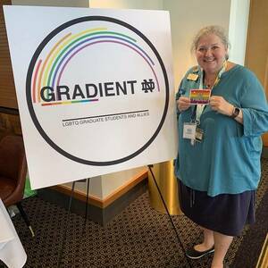 Mimi Beck stands next to a large sign with the GradientND logo holding a rainbow sticker that reads 