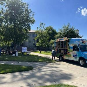 Wide shot of the quad outside Bond Hall. On the right someone is getting shaved ice from a Kona ice food truck and on the left there are several people visible at picnic tables.