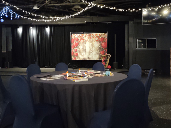 Photo of part of the Legends event room. In the foreground is a table covered in craft supplies and in the background is a stage featuring a heart-themed photo backdrop and a small pink skeleton.